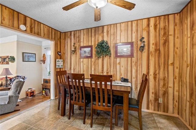 dining area featuring ceiling fan, a textured ceiling, and wooden walls