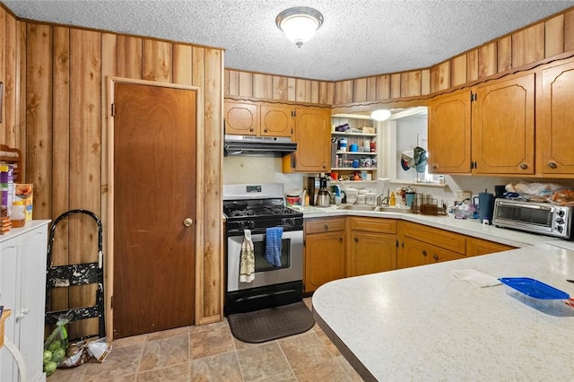 kitchen with stainless steel gas range, sink, wood walls, a textured ceiling, and kitchen peninsula