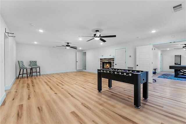 playroom featuring a stone fireplace, light hardwood / wood-style floors, and ceiling fan