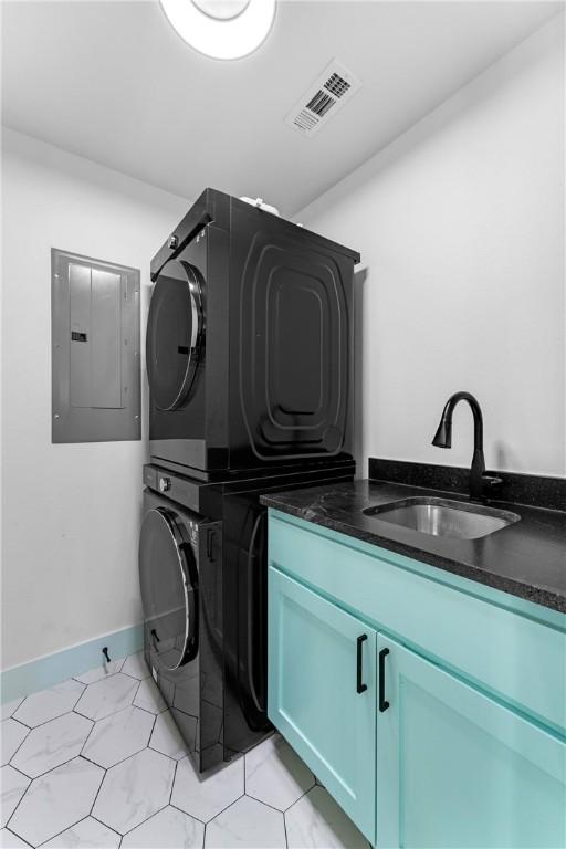 laundry area with cabinets, stacked washing maching and dryer, electric panel, and sink