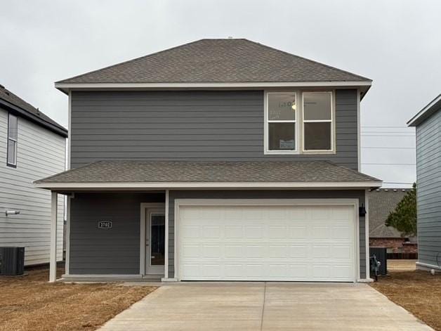 traditional-style house featuring driveway, a garage, central AC, and a shingled roof