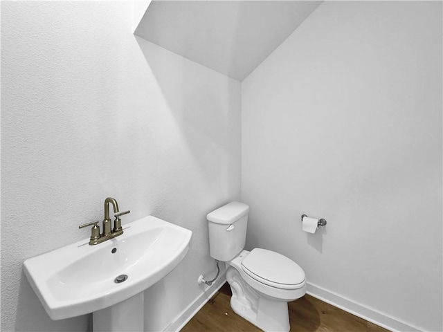 half bath featuring toilet, wood finished floors, baseboards, and a sink