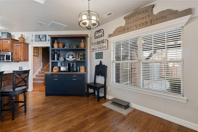 bar with decorative backsplash, dark hardwood / wood-style floors, and a chandelier