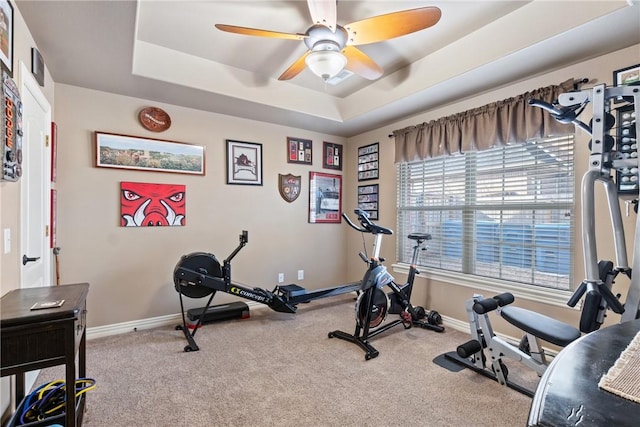 workout area with ceiling fan, light colored carpet, and a tray ceiling