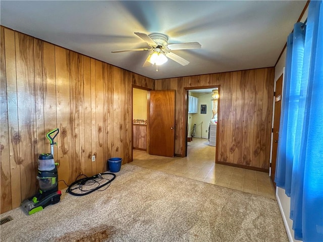 spare room with ceiling fan, light colored carpet, and wooden walls