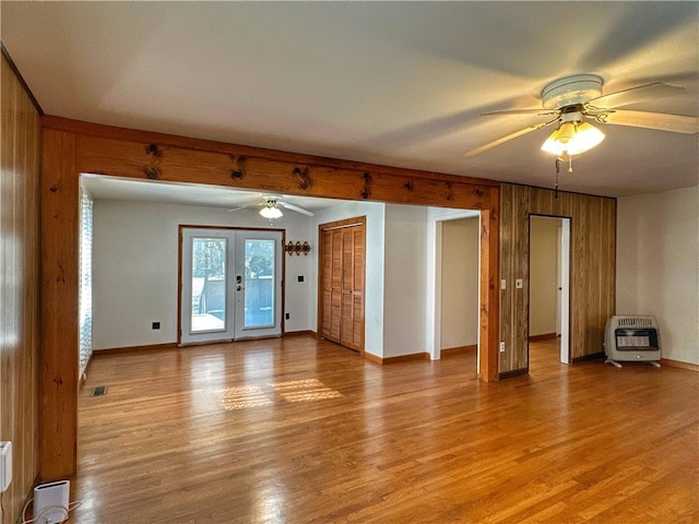 unfurnished living room featuring french doors, heating unit, wood walls, light wood-type flooring, and ceiling fan