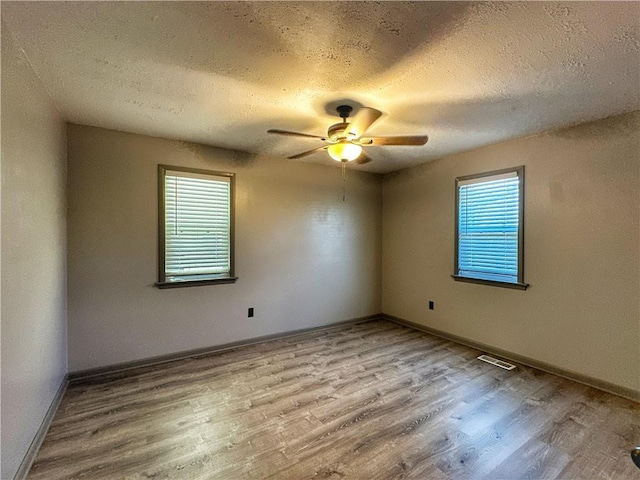 spare room with ceiling fan, plenty of natural light, a textured ceiling, and light wood-type flooring