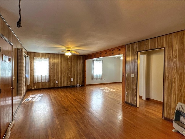 unfurnished living room with heating unit, wood-type flooring, wooden walls, and ceiling fan