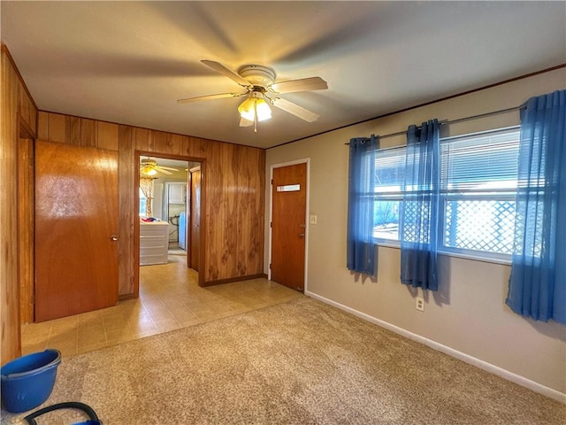 interior space with ceiling fan, light carpet, and wood walls