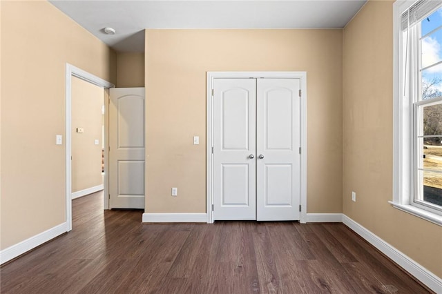 unfurnished bedroom featuring multiple windows, a closet, and dark hardwood / wood-style floors