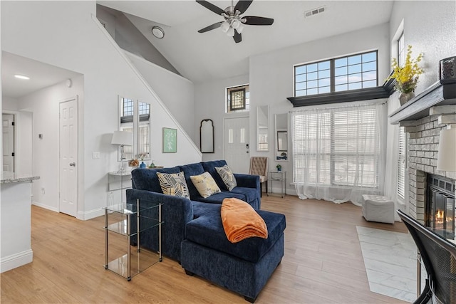 living room featuring a towering ceiling, ceiling fan, a fireplace, and light wood-type flooring