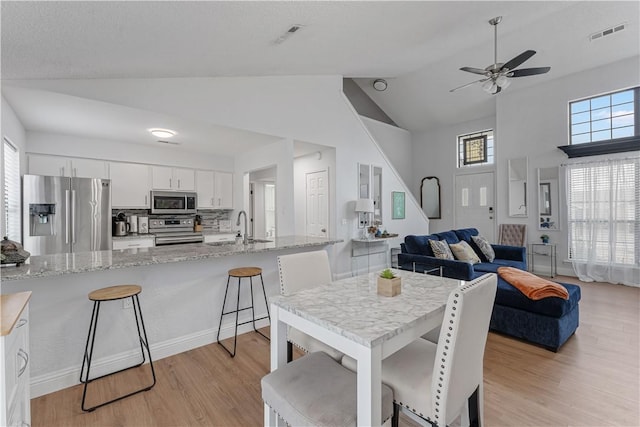 dining area with lofted ceiling, sink, a wealth of natural light, and light hardwood / wood-style floors