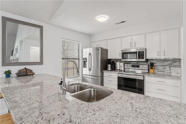 kitchen featuring sink, stainless steel appliances, light stone countertops, white cabinets, and kitchen peninsula