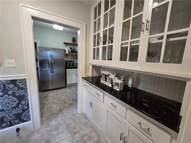 kitchen with stainless steel fridge, dark stone counters, and white cabinets