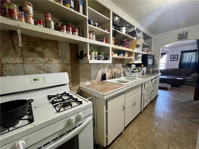 kitchen with light tile patterned flooring, white cabinetry, sink, backsplash, and white gas stove