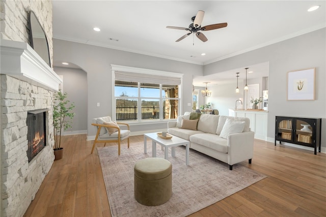 living room featuring hardwood / wood-style flooring, ceiling fan, ornamental molding, and a stone fireplace