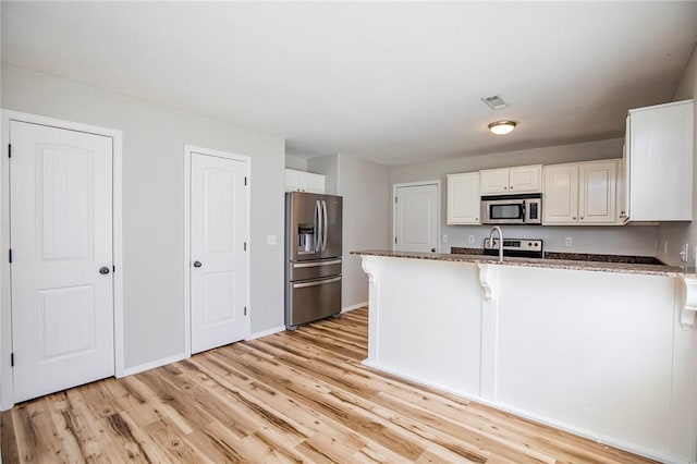 kitchen with appliances with stainless steel finishes, dark stone countertops, white cabinets, kitchen peninsula, and light wood-type flooring