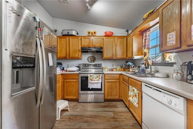 kitchen with vaulted ceiling, appliances with stainless steel finishes, range hood, wood-type flooring, and sink