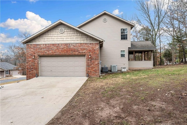 view of front of home with central AC unit, an attached garage, concrete driveway, a sunroom, and brick siding