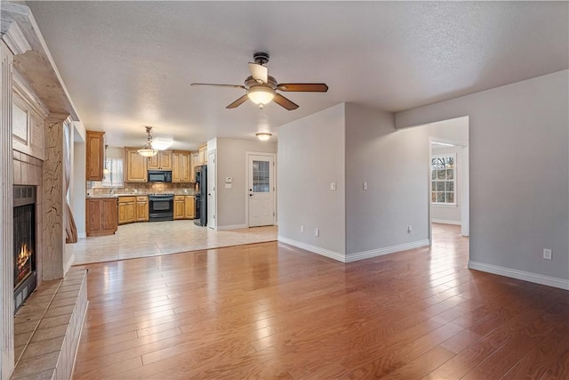 unfurnished living room with a ceiling fan, light wood-style flooring, baseboards, a warm lit fireplace, and a textured ceiling