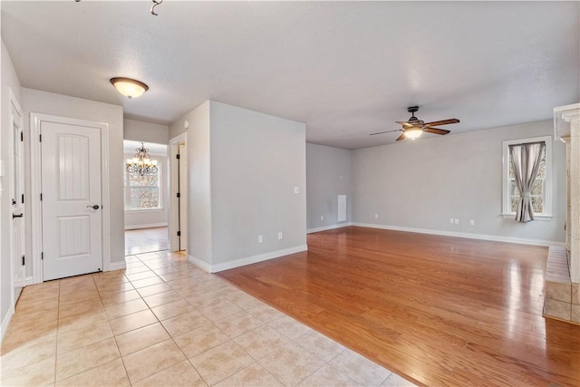 unfurnished room featuring a chandelier, a ceiling fan, light tile patterned floors, and baseboards