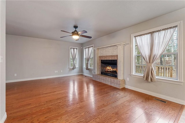 unfurnished living room featuring ceiling fan, wood finished floors, a tiled fireplace, and baseboards
