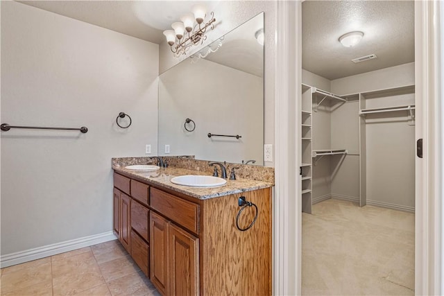 bathroom with a walk in closet, baseboards, double vanity, and a textured ceiling