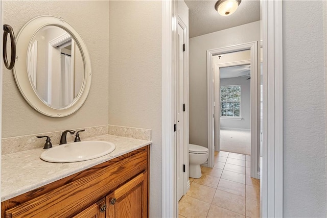 bathroom featuring toilet, tile patterned flooring, vanity, and a textured wall