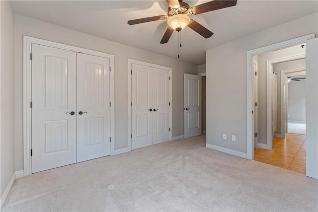 unfurnished bedroom featuring multiple closets, light carpet, baseboards, and ceiling fan