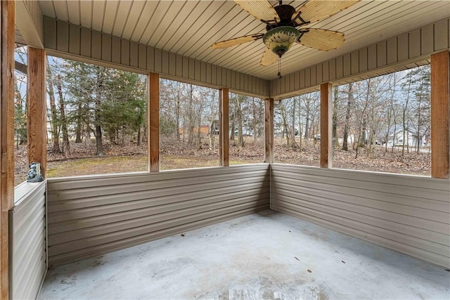 unfurnished sunroom with ceiling fan, view of wooded area, and healthy amount of natural light