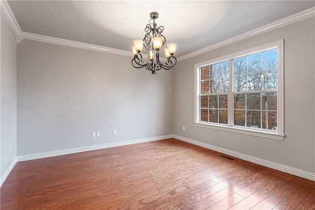 empty room featuring wood finished floors, ornamental molding, a chandelier, and baseboards