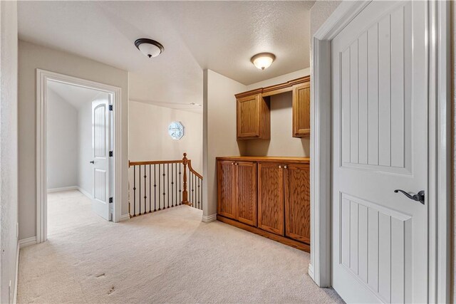 corridor featuring an upstairs landing, light carpet, baseboards, and a textured ceiling