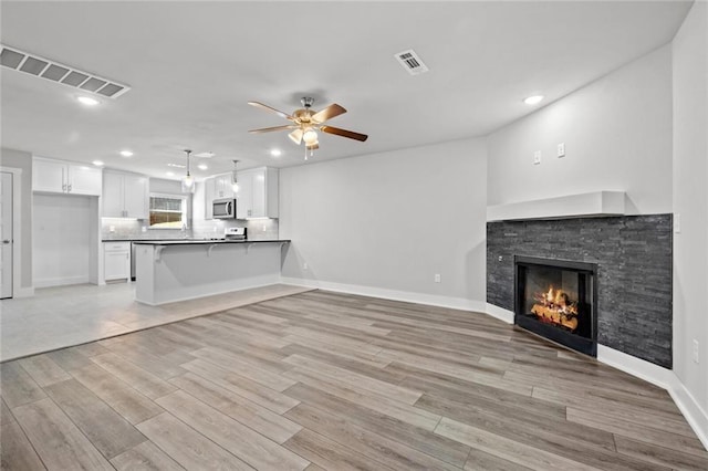 unfurnished living room featuring ceiling fan, a fireplace, and light hardwood / wood-style floors