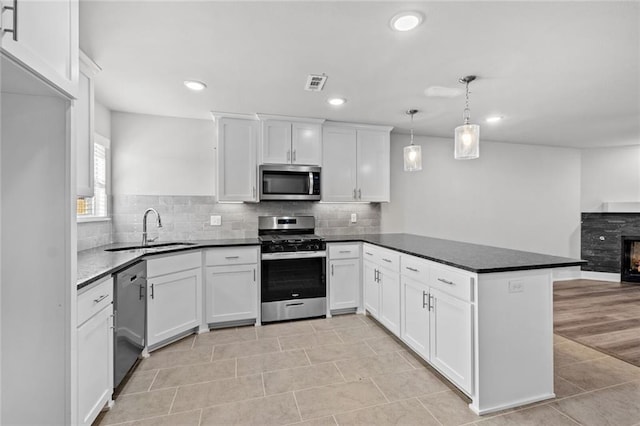 kitchen with appliances with stainless steel finishes, decorative light fixtures, white cabinetry, sink, and kitchen peninsula