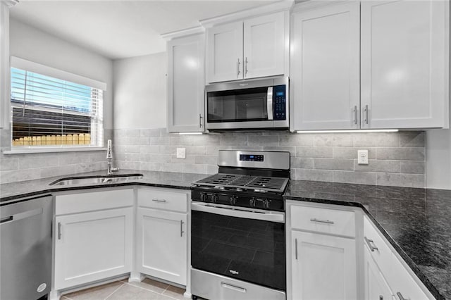 kitchen with sink, dark stone countertops, white cabinets, light tile patterned floors, and stainless steel appliances