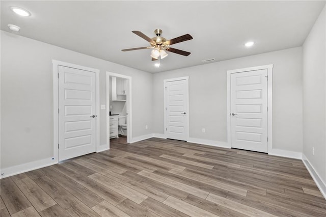 unfurnished bedroom with hardwood / wood-style flooring, ceiling fan, and two closets