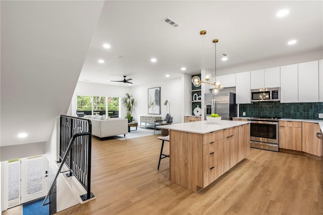 kitchen with white cabinetry, a kitchen island, a kitchen breakfast bar, stainless steel appliances, and hanging light fixtures