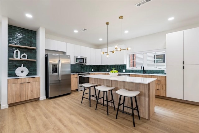 kitchen with appliances with stainless steel finishes, a center island, white cabinetry, light wood-type flooring, and hanging light fixtures