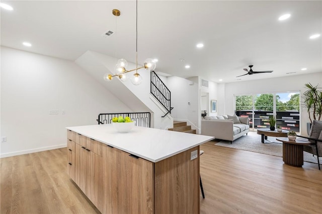 kitchen with ceiling fan, a kitchen island, light hardwood / wood-style floors, and pendant lighting