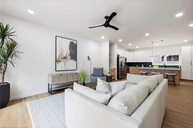 living room with ceiling fan with notable chandelier, light hardwood / wood-style floors, and sink