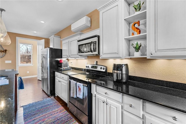 kitchen featuring white cabinetry, decorative light fixtures, a wall mounted AC, appliances with stainless steel finishes, and dark stone counters