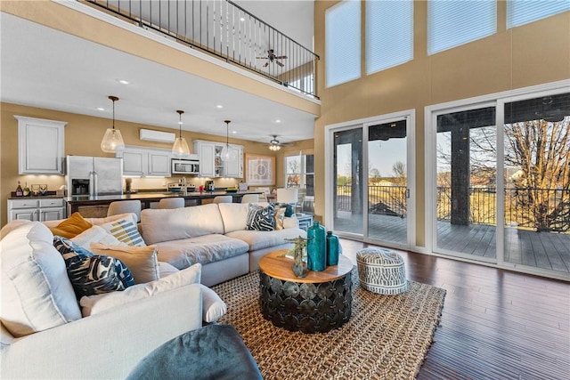 living room with a high ceiling, dark wood-type flooring, a wealth of natural light, and ceiling fan