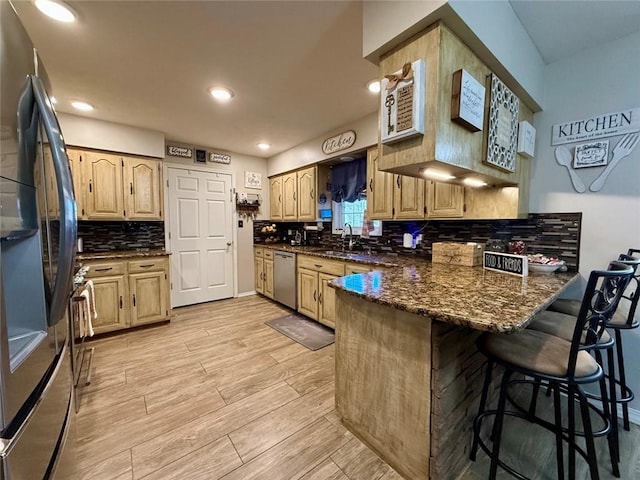 kitchen with sink, light wood-type flooring, dark stone countertops, appliances with stainless steel finishes, and kitchen peninsula