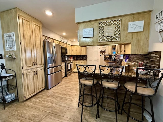 kitchen featuring appliances with stainless steel finishes, light brown cabinetry, tasteful backsplash, sink, and a kitchen breakfast bar