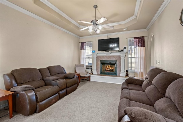 carpeted living room with a tiled fireplace, crown molding, a raised ceiling, and ceiling fan