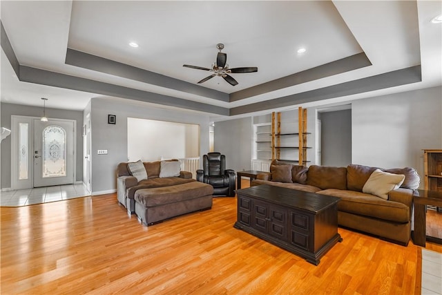 living area with light wood finished floors, baseboards, and a tray ceiling