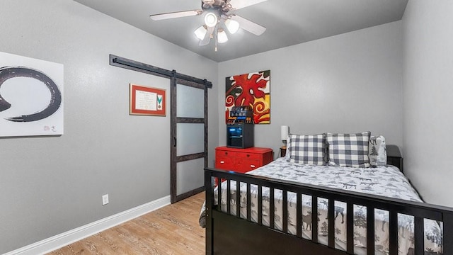 bedroom featuring a barn door, ceiling fan, and light wood-type flooring