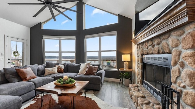 living room with a water view, a stone fireplace, hardwood / wood-style floors, and high vaulted ceiling