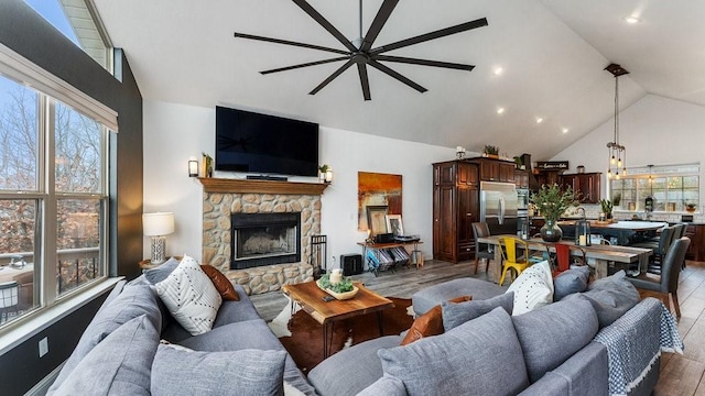 living room with high vaulted ceiling, a stone fireplace, a wealth of natural light, and light hardwood / wood-style floors