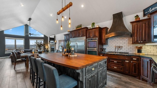 kitchen with a kitchen island, appliances with stainless steel finishes, pendant lighting, butcher block counters, and custom range hood